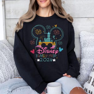 May include: Black sweatshirt with a colorful Disney Family Trip 2020 graphic. The design features Mickey Mouse ears, fireworks, and a castle silhouette. The text is in pink, blue, and yellow.