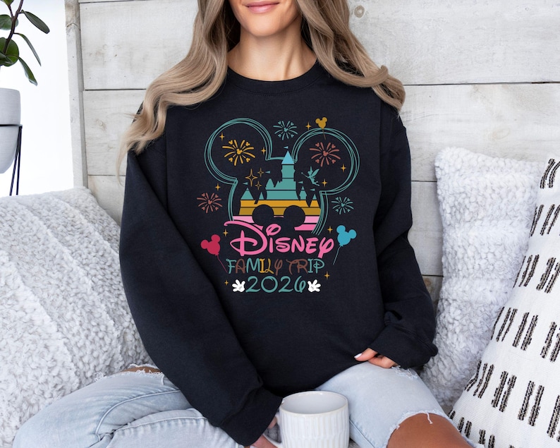 May include: Black sweatshirt with a colorful Disney Family Trip 2020 graphic. The design features Mickey Mouse ears, fireworks, and a castle silhouette. The text is in pink, blue, and yellow.