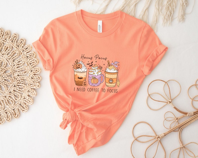 May include: Orange t-shirt with a graphic of three Halloween-themed coffee drinks with the text "Hocus Pocus I need coffee to focus".