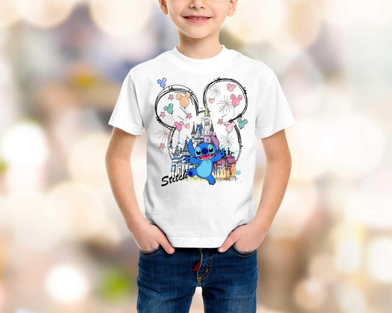 May include: White t-shirt featuring a colorful graphic of the character Stitch from Lilo & Stitch. The design includes a castle, fireworks, and the word "Stitch". The graphic is set within a Mickey Mouse ear outline.