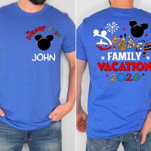 May include: Blue t-shirt with "Disney 2026" and a Mickey Mouse head graphic on the front. The name "JOHN" is printed below. The back features "Disney Family Vacation 2026" with character illustrations and fireworks.
