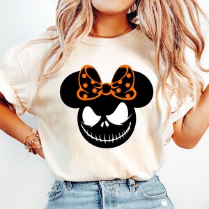 Puede incluir: Camiseta color crema con un gr&aacute;fico negro y naranja. El gr&aacute;fico combina elementos de Mickey Mouse y Jack Skellington de Pesadilla antes de Navidad. El dise&ntilde;o incluye un lazo con lunares y una sonrisa siniestra.