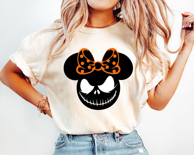 Puede incluir: Camiseta color crema con un gr&aacute;fico negro y naranja. El gr&aacute;fico combina elementos de Mickey Mouse y Jack Skellington de Pesadilla antes de Navidad. El dise&ntilde;o incluye un lazo con lunares y una sonrisa siniestra.