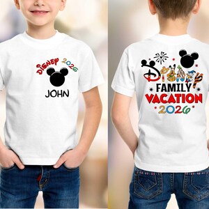 May include: White t-shirt with a colorful Disney design. The front features the text "Disney 2026" with a Mickey Mouse head and the name "JOHN". The back of the shirt says "Disney Family Vacation 2026" with Disney characters.