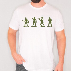 May include: White t-shirt featuring a green graphic of four toy soldiers in different poses. The soldiers are silhouetted, with one holding a gun, another saluting, one with a weapon raised, and the last with a rifle.