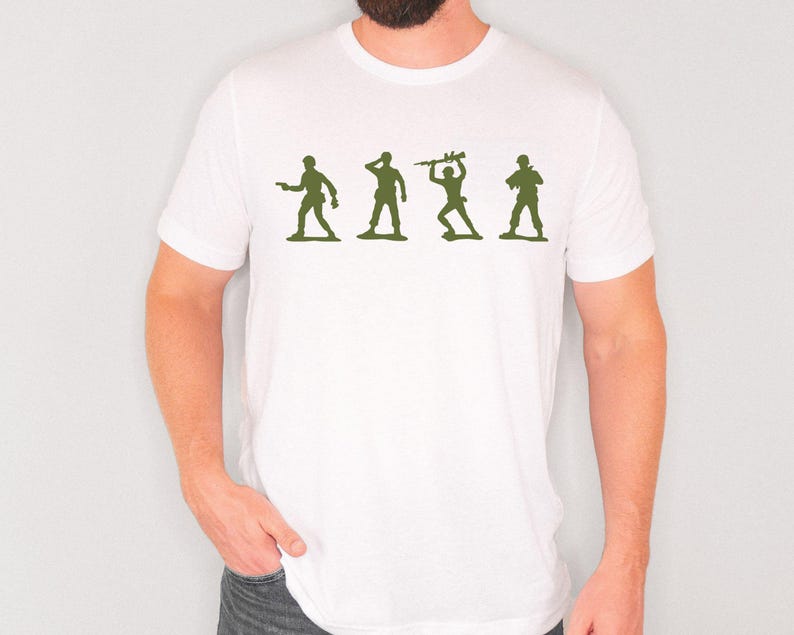 May include: White t-shirt featuring a green graphic of four toy soldiers in different poses. The soldiers are silhouetted, with one holding a gun, another saluting, one with a weapon raised, and the last with a rifle.