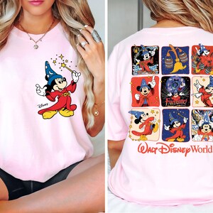 May include: Light pink t-shirt featuring a graphic of Mickey Mouse as a wizard on the front. The back of the shirt displays a grid of Mickey Mouse images and the words "Walt Disney World".
