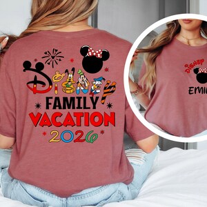 May include: A maroon t-shirt featuring a Disney-themed design. The back of the shirt displays the text "Disney Family Vacation 2026" with Mickey Mouse and friends. The front of the shirt has a smaller design with the name "Emily".