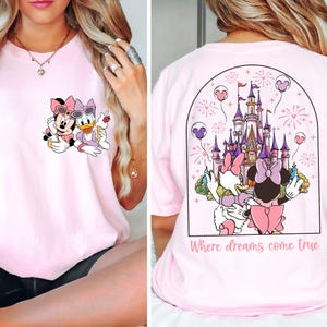 May include: Pink t-shirt with a graphic of Minnie Mouse and Daisy Duck on the front and a graphic of Cinderella's castle with Minnie Mouse and Daisy Duck on the back. The text "Where dreams come true" is printed on the back of the shirt.