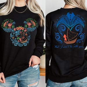 Puede incluir: Sudadera negra de manga larga con un dise&ntilde;o gr&aacute;fico colorido. La parte delantera muestra una cabeza de Mickey Mouse con motivos florales y de barco, y el texto "COME WHAT MAY" y "I KNOW THE WAY". La parte trasera tiene un dise&ntilde;o de barco y el texto "There's nowhere you can go that I won't be with you."