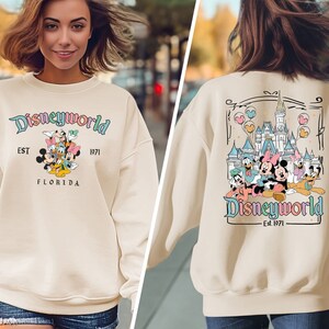 May include: A cream-coloured sweatshirt with the text "Disneyworld" and various cartoon characters. The sweatshirt also features the text "EST 1971 FLORIDA". The back of the sweatshirt has a castle graphic and the text "Disneyworld Est. 1971".