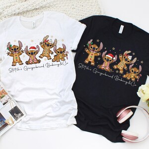 Puede incluir: Dos camisetas, una blanca y otra negra, cada una con un dise&ntilde;o de dibujos animados de personajes estilo pan de jengibre. Los personajes est&aacute;n decorados con accesorios tem&aacute;ticos navide&ntilde;os. El texto "Stitch's Gingerbread Baking & Co" est&aacute; impreso debajo.
