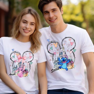 May include: Two white t-shirts featuring a Mickey Mouse head design with fireworks and a castle. One shirt has a pink bow and the word "Angel", the other has Stitch and the word "Stitch".
