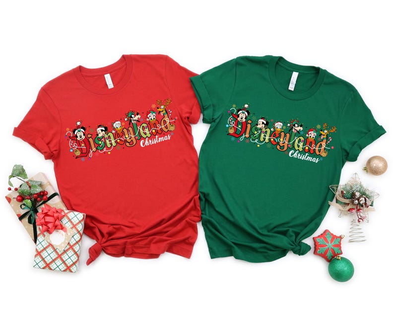 May include: Two short-sleeved t-shirts, one red and one green, featuring a festive "Disneyland Christmas" design. The design includes cartoon characters and holiday lights. The shirts are displayed on a white background with Christmas decorations.
