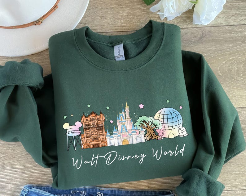 May include: Dark green sweatshirt featuring a colorful graphic of Walt Disney World landmarks, including Cinderella's castle and Spaceship Earth. The words "Walt Disney World" are written in a script font below the graphic.