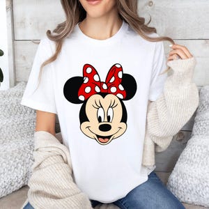 May include: White t-shirt with a black and white cartoon image of Minnie Mouse wearing a red bow with white polka dots.