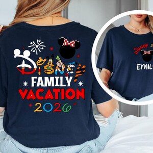 May include: Navy blue t-shirt with a Disney theme. The back features Mickey Mouse, Minnie Mouse, Donald Duck, and Goofy graphics, along with the text "Family Vacation 2026." The front has a smaller design with "Disney 2026" and a name.
