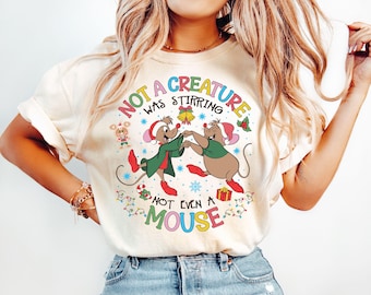 May include: A white t-shirt with a Christmas-themed graphic featuring two mice dancing. The text on the shirt reads "Not a creature was stirring not even a mouse".