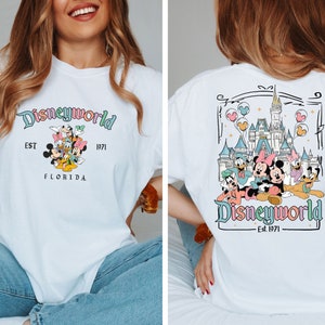 May include: White t-shirt with a Disneyworld design. The front has the text "Disneyworld" in pastel colours, with Mickey Mouse, Minnie Mouse, Donald Duck, Daisy Duck, and Goofy. The back shows the Disney castle and characters.