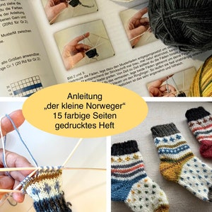 Könnte beinhalten: Nahaufnahme eines Strickprojekts, ein Paar bunte Socken mit weißem Hintergrund und blauem, rotem und gelbem Muster. Die Socken liegen auf einer weißen Oberfläche. Das Bild zeigt auch eine Seite aus einem Strickmusterbuch mit dem Titel "Anleitung "der kleine Norweger" 15 farbige Seiten gedrucktes Heft".