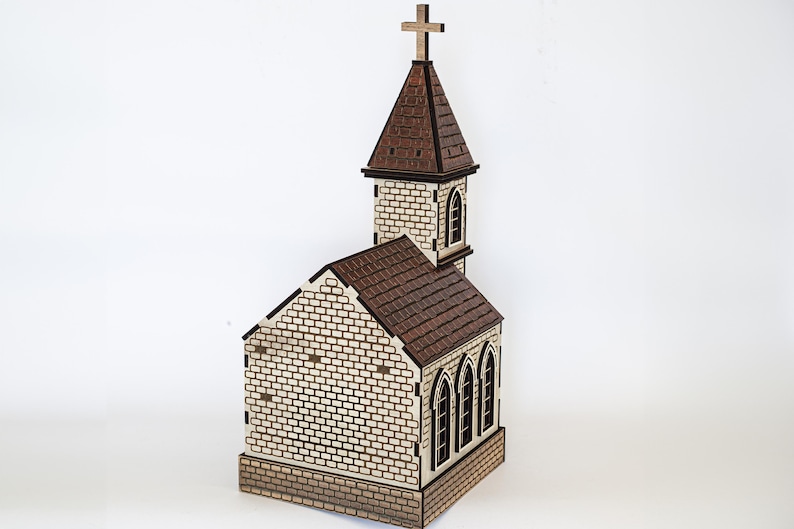 K&ouml;nnte beinhalten: Ein Holzmodell einer Kirche mit einem braunen Dach und einer wei&szlig;en Backsteinfassade. Die Kirche hat einen hohen Turm mit einem Kreuz auf der Spitze. Das Modell ist detailliert mit Fenstern und einer T&uuml;r.