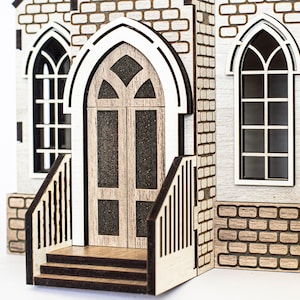 K&ouml;nnte beinhalten: Ein Holzmodell einer Kirche mit einer braunen T&uuml;r, zwei Fenstern und einer Backsteinfassade. Die Kirche hat einen kleinen Vorbau mit Stufen, die zur T&uuml;r f&uuml;hren.