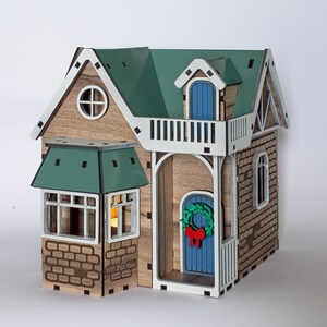 May include: A wooden model house with a green roof, white trim, and a blue door. The house has a small balcony with a white railing and a wreath on the door.