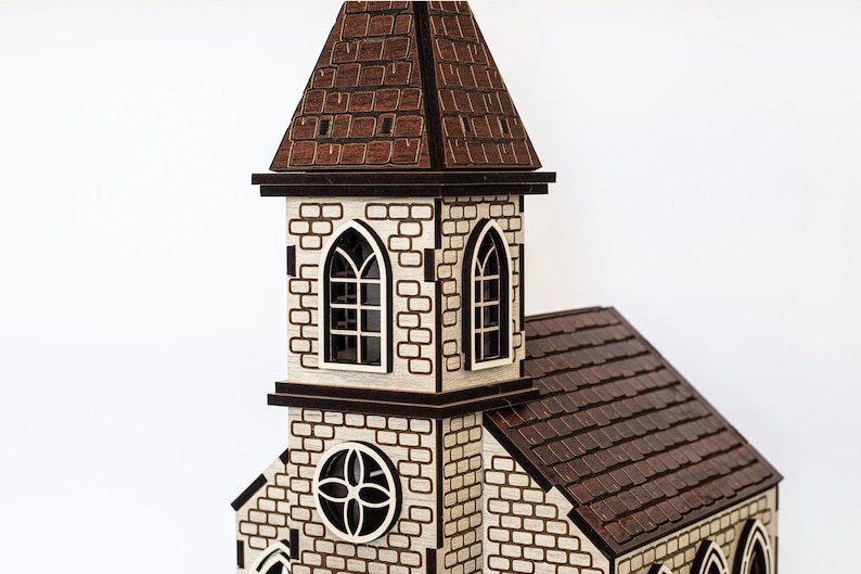 K&ouml;nnte beinhalten: Ein Holzmodell einer Kirche mit einem braunen Dach und wei&szlig;en Backsteinmauern. Die Kirche hat einen hohen Turm mit einem spitzen Dach und zwei Bogenfenstern. Im unteren Bereich des Turms befindet sich ein rundes Fenster mit einem dekorativen Muster.