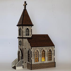 K&ouml;nnte beinhalten: Ein Holzmodell einer Kirche mit braunem Dach, wei&szlig;en Backsteinw&auml;nden und Fenstern, durch die Licht scheint. Die Kirche hat einen hohen Turm mit einem Kreuz auf der Spitze.