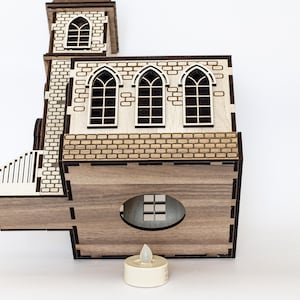 K&ouml;nnte beinhalten: Ein Holzmodell einer Kirche mit brauner gebeizter Oberfl&auml;che. Die Kirche hat drei Fenster und eine kleine Veranda. Ein wei&szlig;es LED-Teelicht steht vor der Kirche.