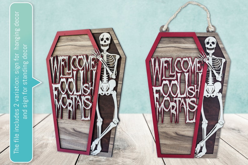 May include: Wooden coffin-shaped sign with a red border and the words "WELCOME FOOLISH MORTALS" in white. A skeleton figure is positioned on the right side. The sign includes a rope for hanging.