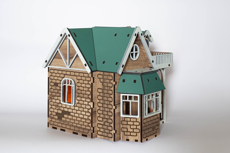 May include: A wooden model house with a green roof, white trim, and brick detailing. The house has multiple windows and a small balcony.
