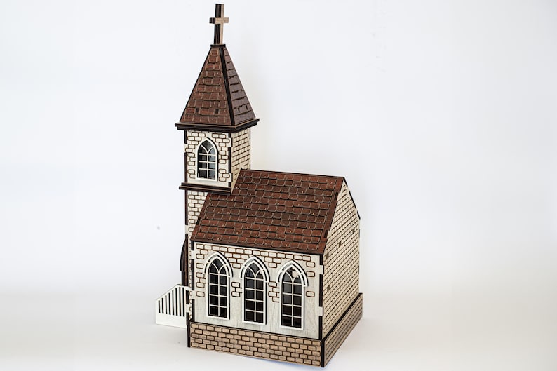 K&ouml;nnte beinhalten: Ein Holzmodell einer kleinen Kirche mit braunem Dach und wei&szlig;en Backsteinw&auml;nden. Die Kirche hat einen Turm mit einem Kreuz auf der Spitze und drei Fenster an der Vorderseite.