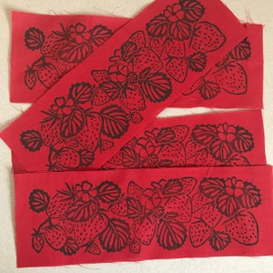 May include: Four red fabric strips with a black print of strawberries and leaves. The fabric is a red color with a black print of strawberries and leaves.