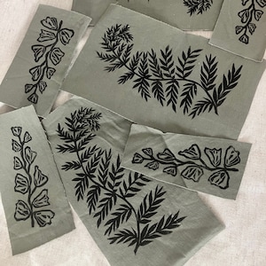 May include: A set of fabric scraps with black fern and flower designs printed on a green background. The fabric scraps are cut into different shapes and sizes.