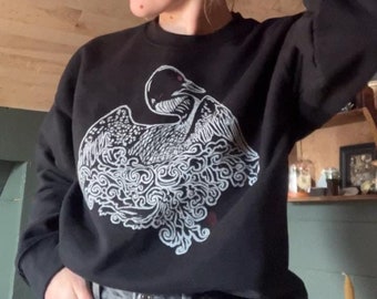 May include: Black sweatshirt with a white graphic print of a bird with outstretched wings surrounded by stylized clouds.