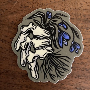 May include: A sticker featuring a hand skeleton with blue flowers growing from it. The flowers are stylized and have a dark blue color. The background is a muted green.