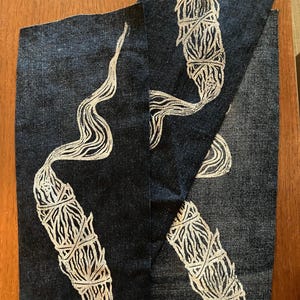 May include: Two white printed designs of smudge sticks on a dark blue fabric background.