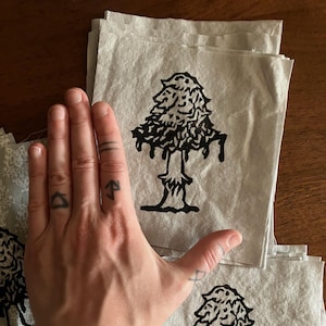 May include: A stack of light gray paper sheets, each featuring a black tree design. The tree has a detailed, textured crown and a slender trunk. The image is taken from a slightly elevated angle, showcasing the stacked sheets.