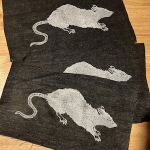 May include: Three black fabric patches with white embroidered images of rats. The rats are in different poses, one is running, one is lying down, and one is curled up.