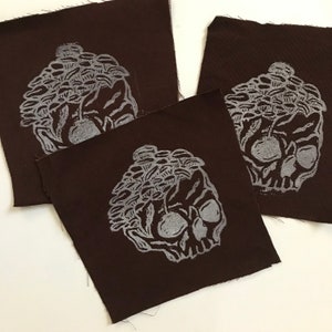 May include: Three brown fabric patches with a white skull design. The skull is topped with a cluster of mushrooms.