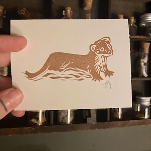 May include: A brown linocut print of a weasel or ferret on a white background. The print is signed in the bottom right corner.