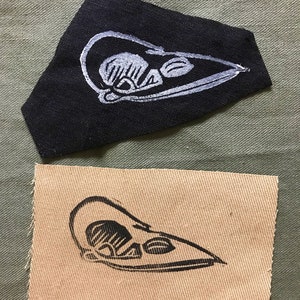 May include: Two fabric patches with a white outline of a bird skull printed on them. The top patch is black and the bottom patch is beige.