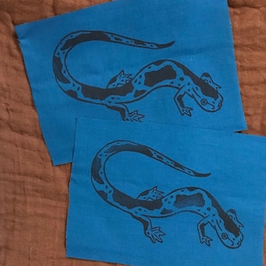 May include: Two blue fabric squares with a black and white salamander design printed on each.