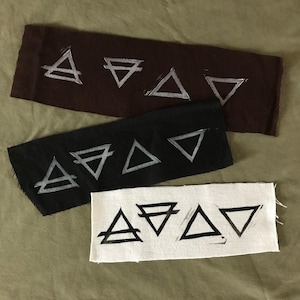 May include: Three fabric strips with four different versions of the four elements symbols. The symbols are printed in white on a brown strip, silver on a black strip, and black on a white strip.