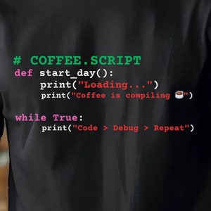 Puede incluir: Una camiseta negra con un diseño humorístico de código de programación. El código está escrito en una fuente verde, roja y rosa e incluye el texto "#COFFEE.SCRIPT" y "Coffee is compiling".
