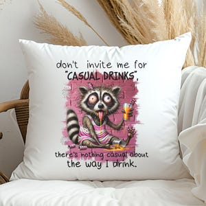 May include: White throw pillow with a humorous illustration of a raccoon drinking from a glass. The text reads "don't invite me for "CASUAL DRINKS", there's nothing casual about the way I drink."