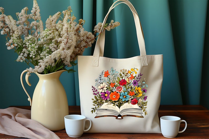 K&ouml;nnte beinhalten: Eine beige Tragetasche mit einem bunten Blumendesign, das auf der Vorderseite aufgedruckt ist. Die Blumen sind um ein offenes Buch mit sichtbaren Seiten angeordnet. Die Tasche hat zwei Henkel.