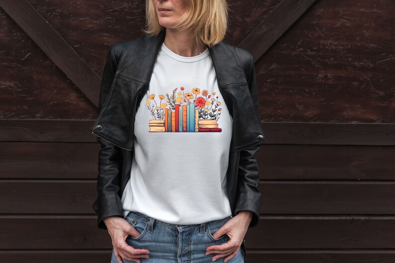 K&ouml;nnte beinhalten: Wei&szlig;es T-Shirt mit einem Aufdruck einer Stapel bunter B&uuml;cher, aus denen Blumen wachsen.