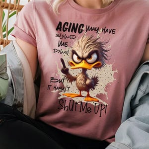May include: A pink t-shirt with a cartoon duck design and the text "Aging may have slowed me down, but it hasn't shut me up!"